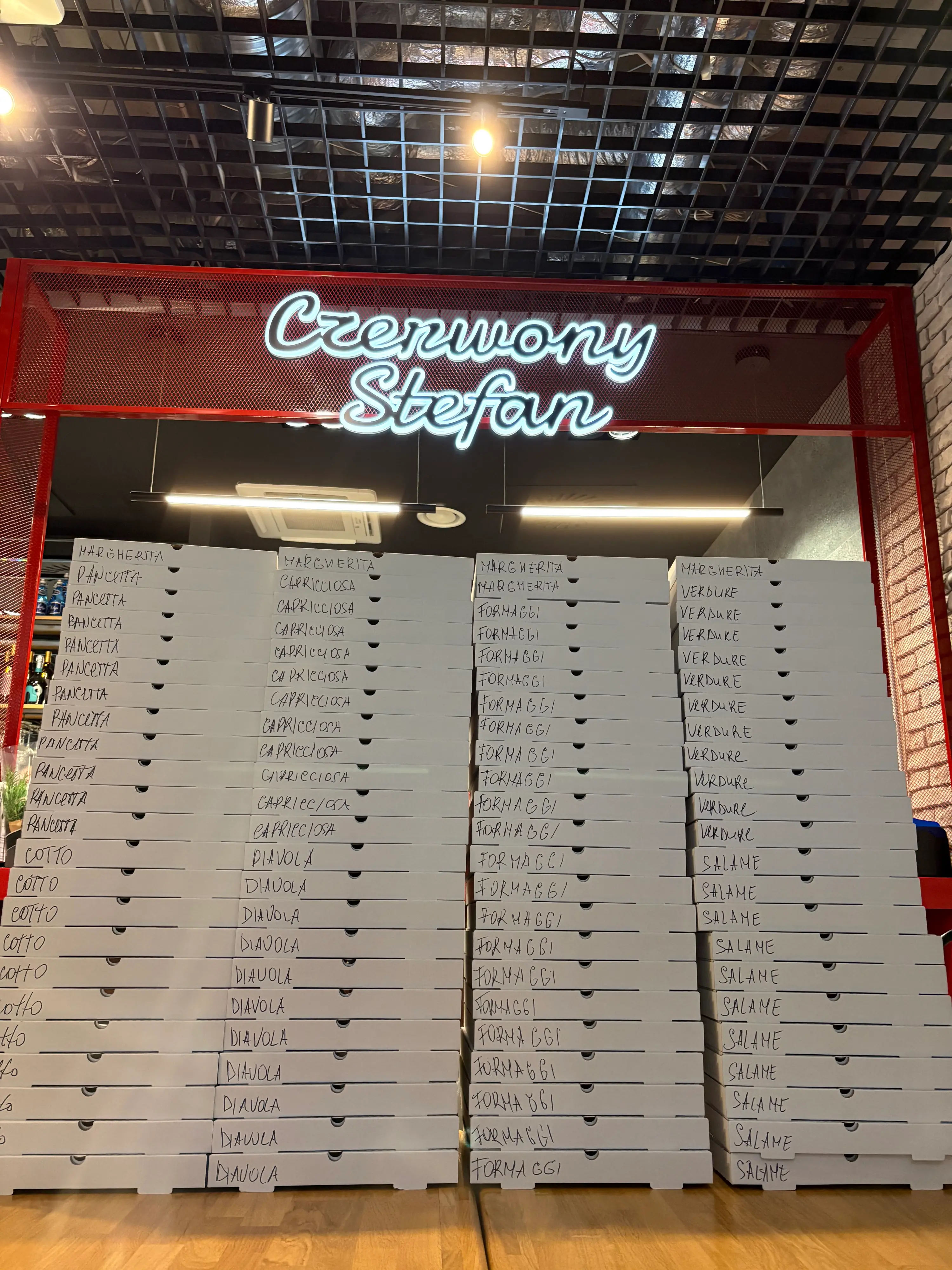 Setki opisanych kartonów z pizzą przygotowanych do dużego zamówienia firmowego w Pizzerii Czerwony Stefan na Woli