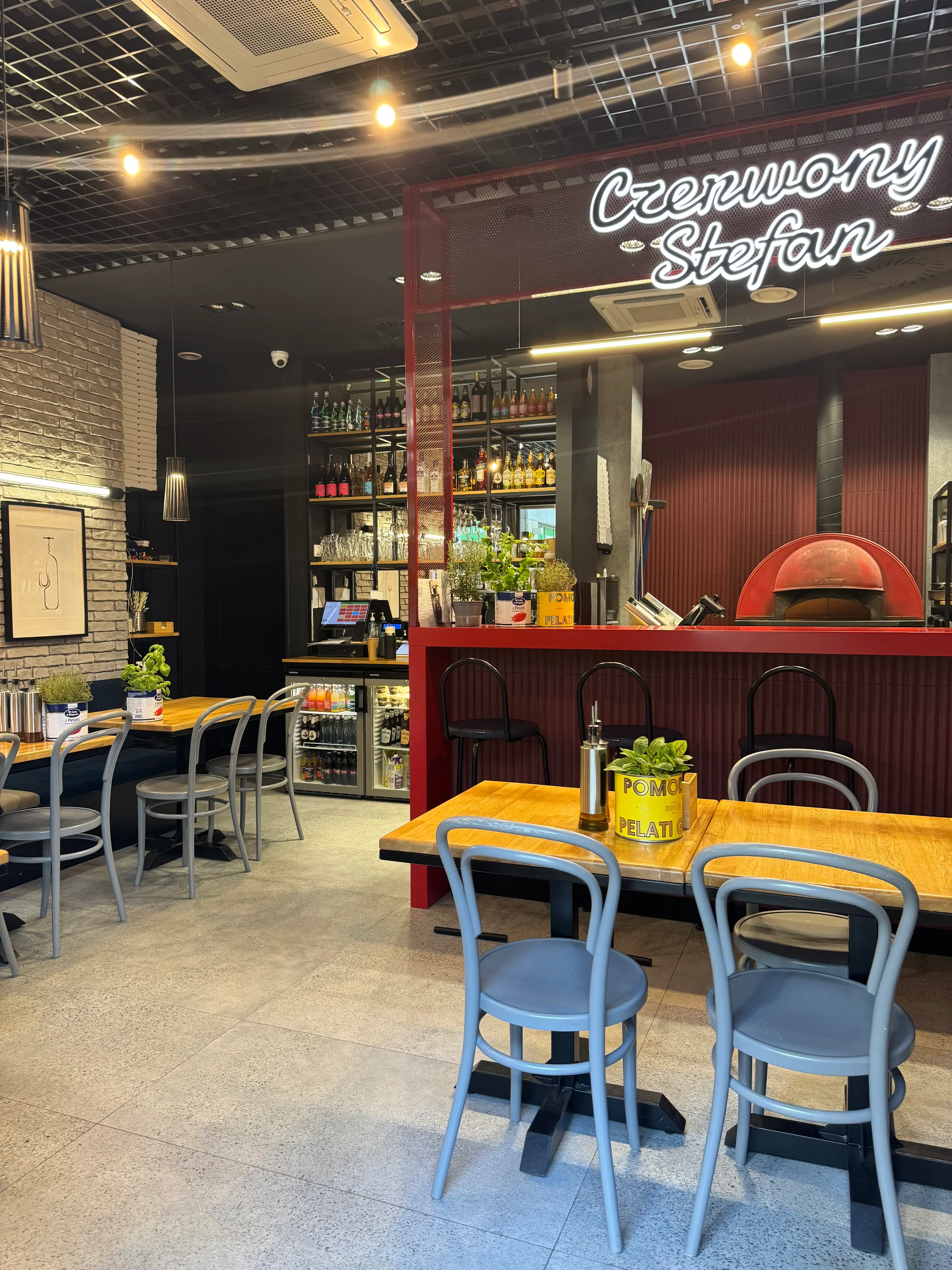 Wnętrze Pizzerii Czerwony Stefan na Woli — sala z neonem, stolikami i czerwonym piecem do pizzy neapolitańskiej