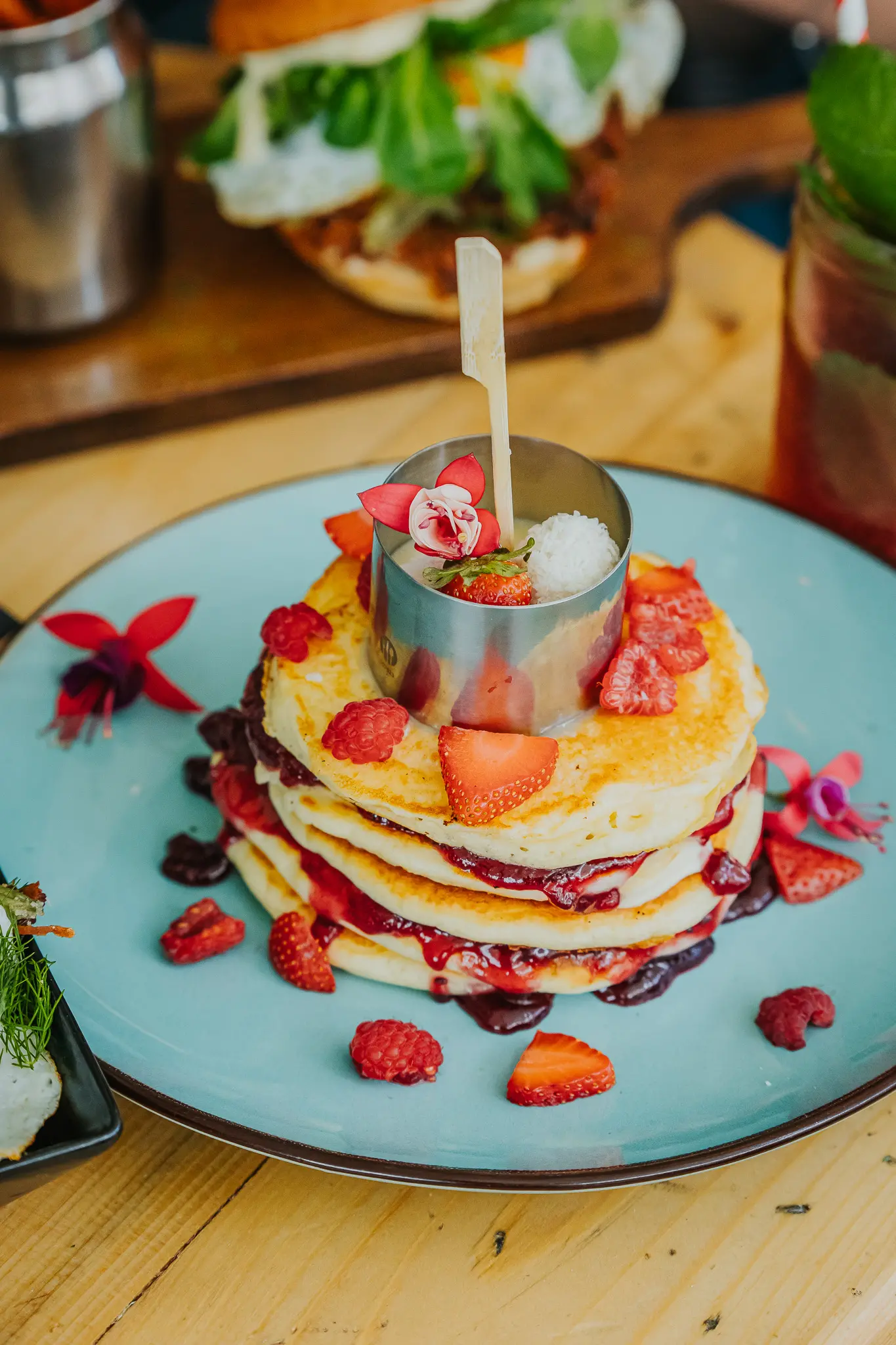 Pancakes ze świezymi truskawkami i sosem podane na niebieskim, ceramicznym talerzu.